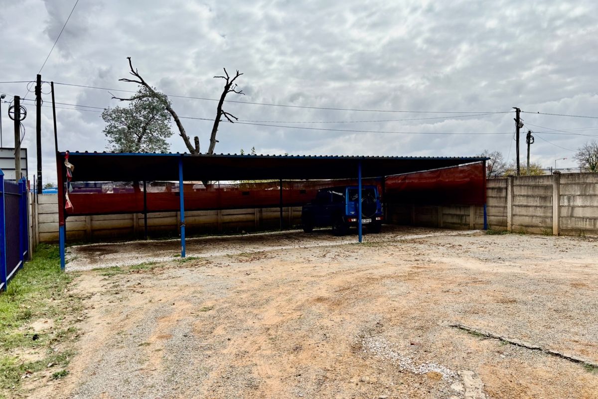 Outdoor parking area featuring a covered metal carport structure with gravel surfacing and perimeter boundary walling.