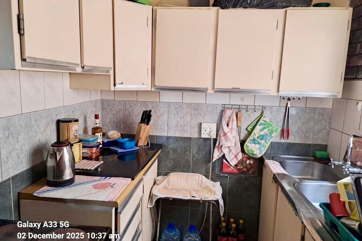 A compact kitchen area featuring built-in cabinetry, a double stainless steel sink, and tiled splashbacks, providing functional workspace for daily operations.