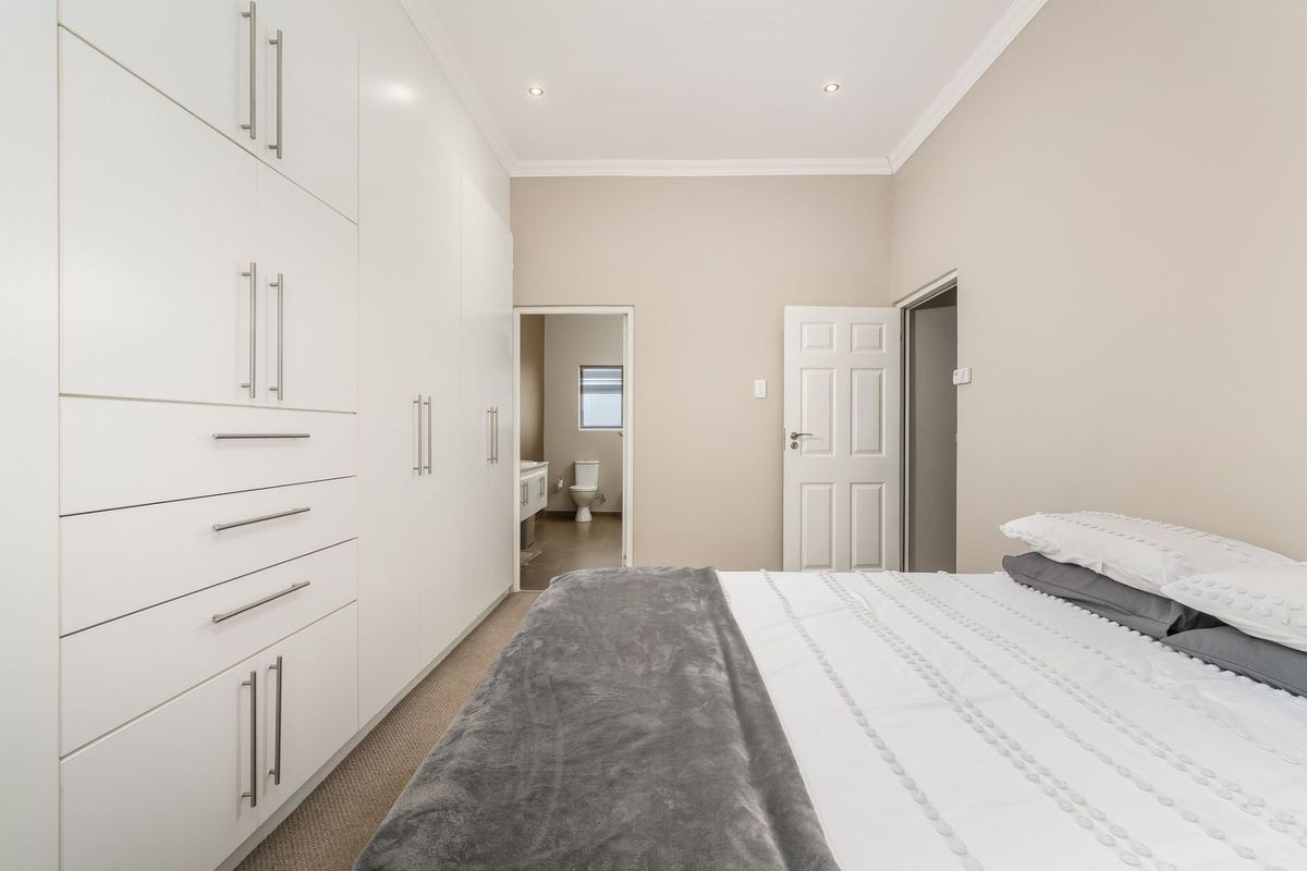 A well-maintained bedroom featuring extensive built-in white cabinetry, recessed lighting, and direct access to an en-suite bathroom.