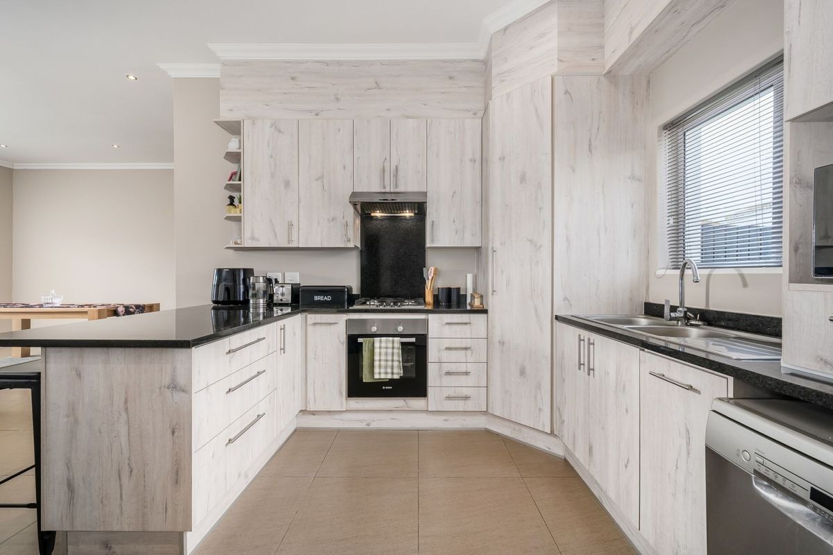 Modern kitchen featuring light wood-grain cabinetry, dark granite countertops, integrated stainless steel appliances, and tiled flooring in an open-plan layout.