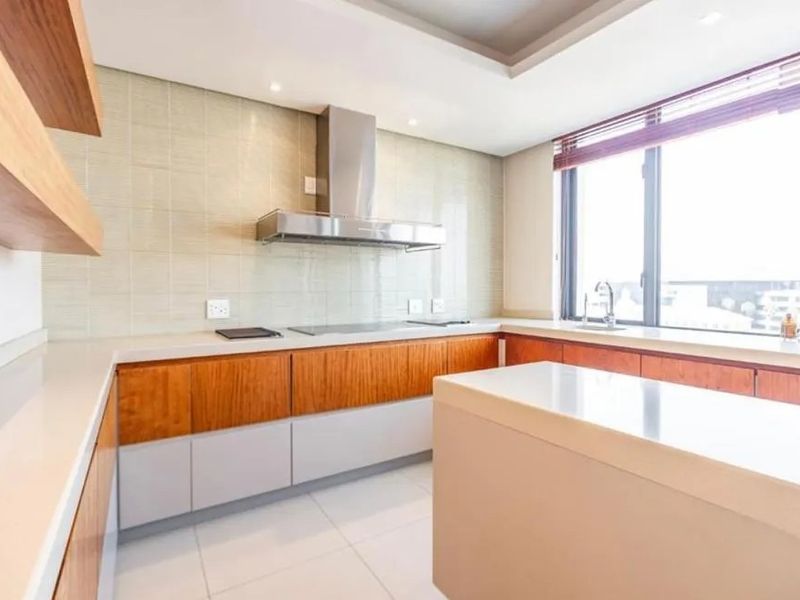 Modern kitchen featuring sleek two-tone cabinetry, stone countertops, a built-in hob, stainless steel extractor fan, and large windows providing ample natural light.