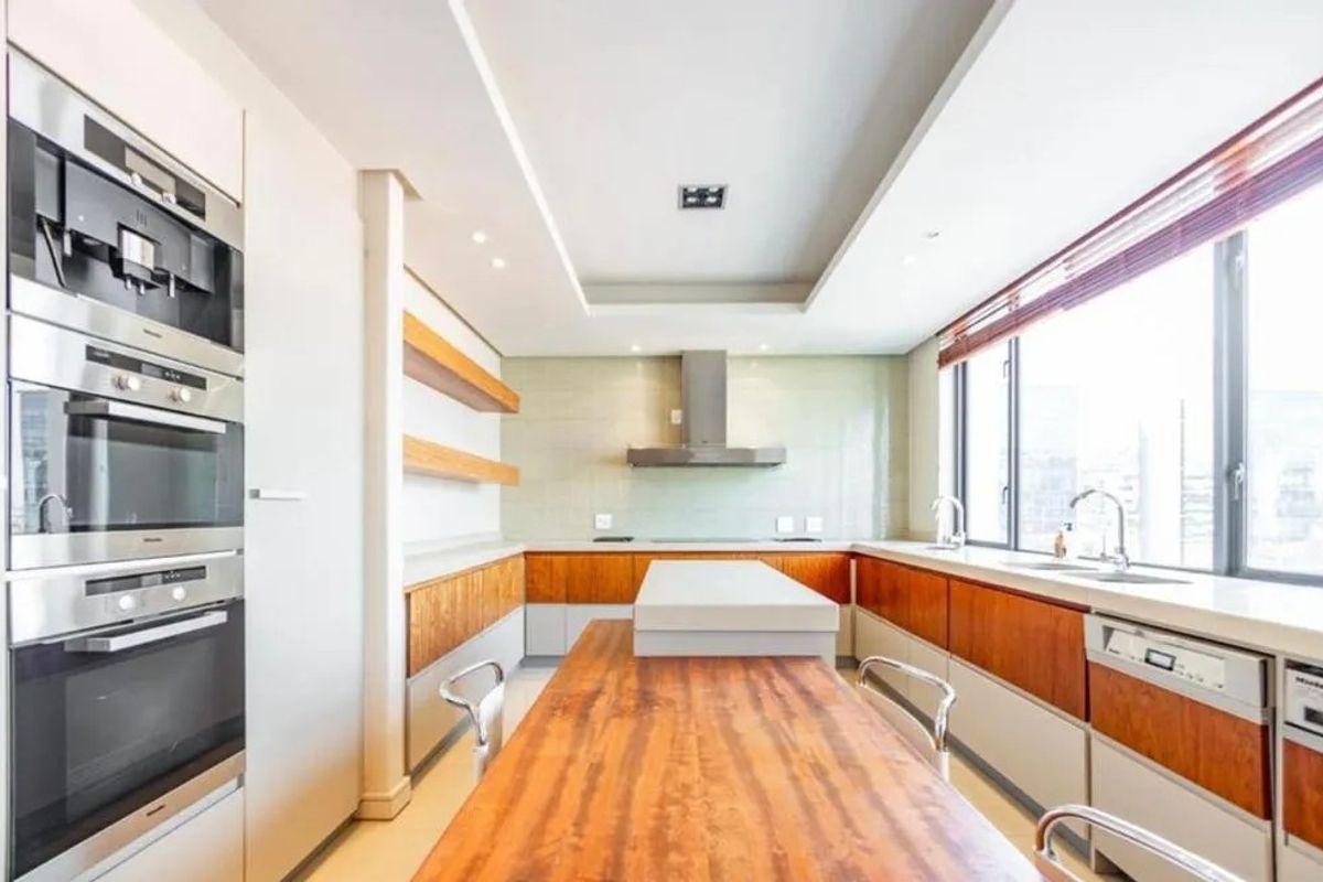 Modern kitchen featuring high-end integrated Miele appliances, sleek wooden cabinetry, stone countertops, and a central island with a breakfast bar.