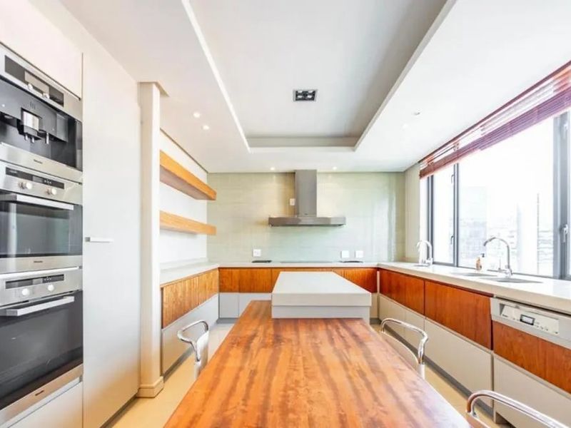 Modern kitchen featuring high-end integrated Miele appliances, sleek wooden cabinetry, stone countertops, and a central island with a breakfast bar.