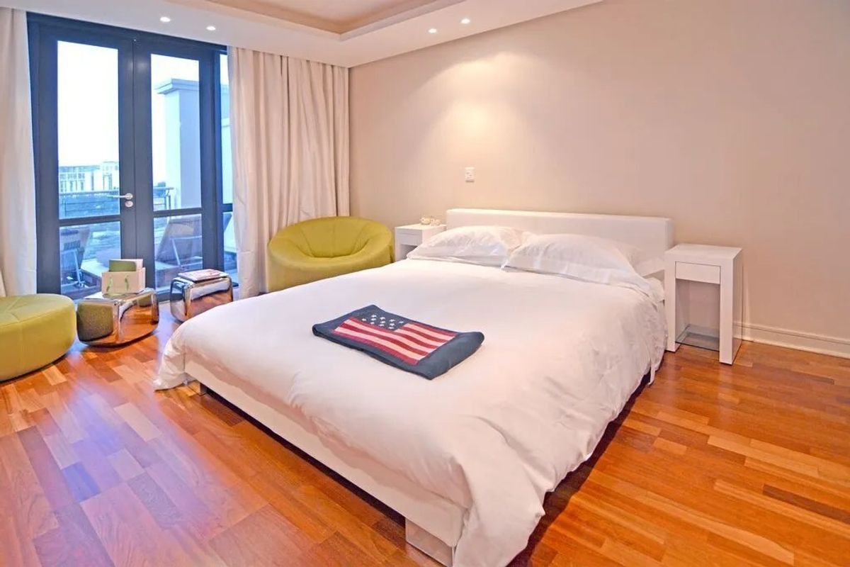 Spacious bedroom featuring warm hardwood flooring, recessed ceiling lighting, and direct access to a private balcony through large glass doors.