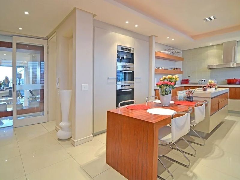 Modern open-plan kitchen featuring a central island with breakfast bar, built-in ovens, sleek cabinetry, and recessed lighting, seamlessly flowing into the living area.