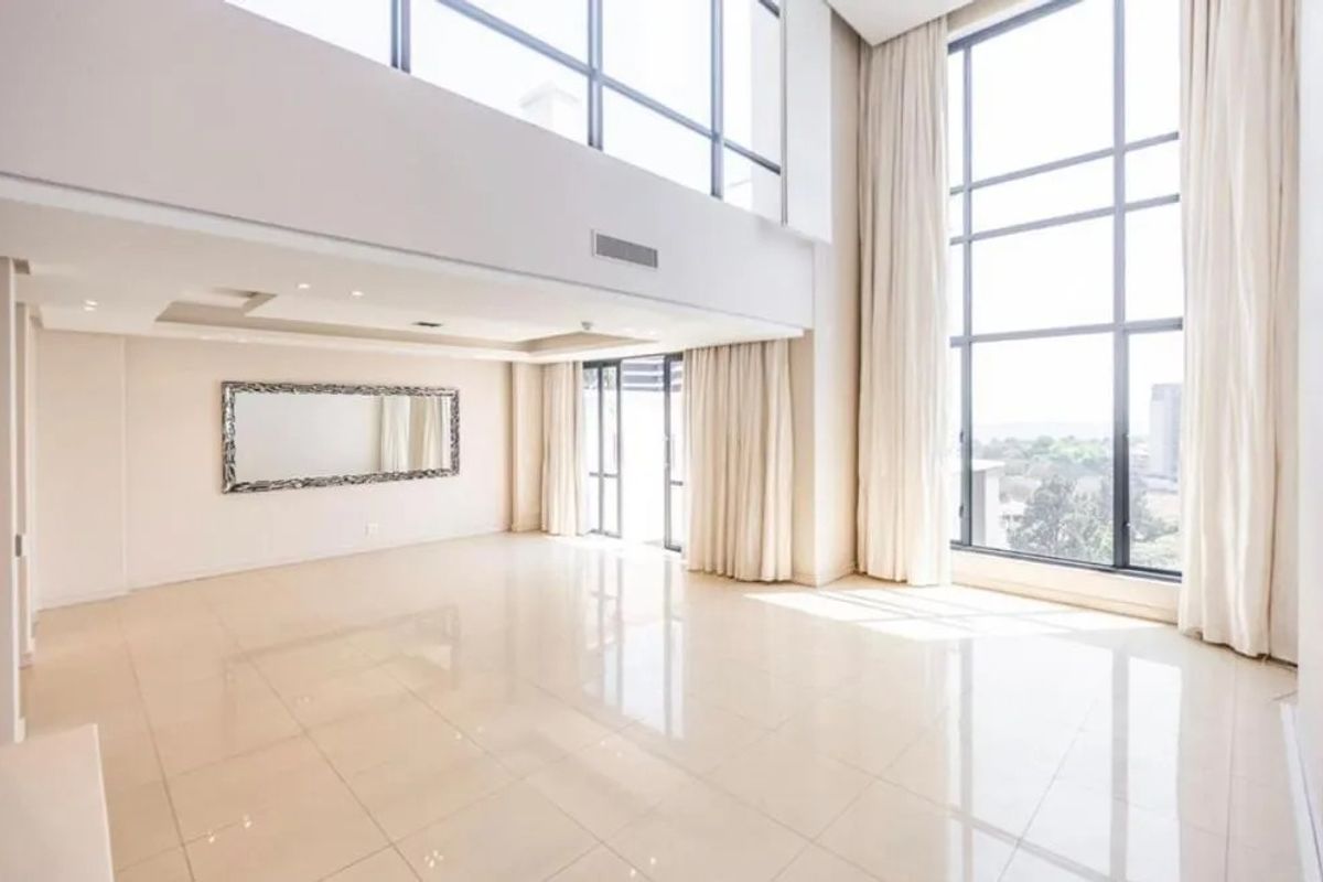 Spacious double-volume living area featuring floor-to-ceiling windows, polished tile flooring, and recessed ceiling lighting in a modern penthouse setting.