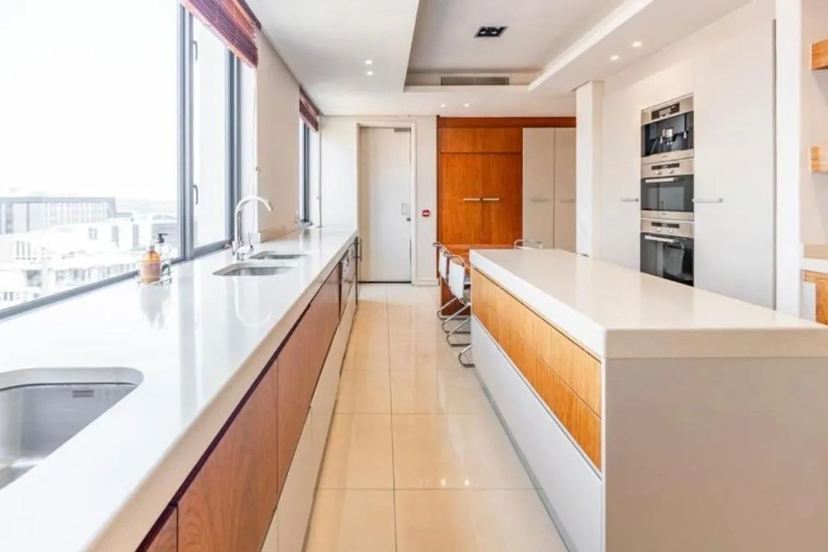 Modern penthouse kitchen featuring sleek white countertops, integrated cabinetry, built-in oven and microwave, and large windows offering expansive city views.