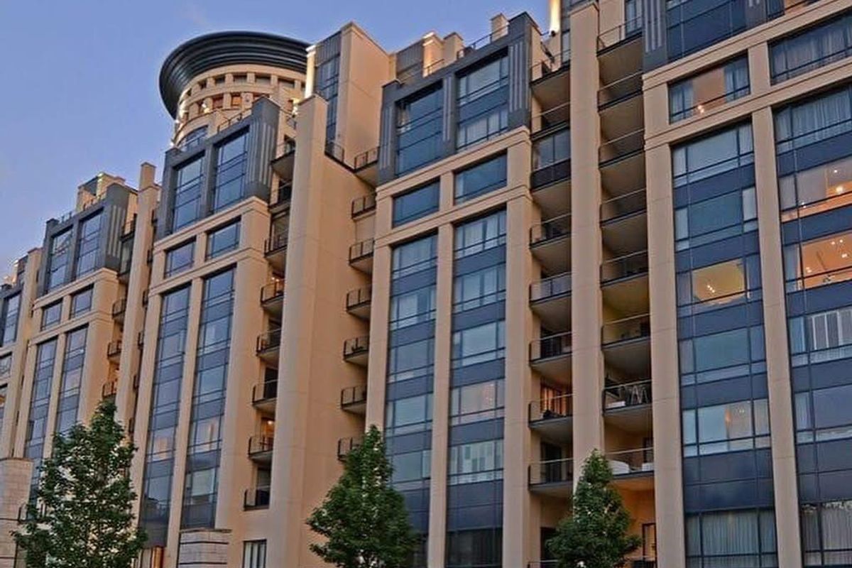 A view of the modern penthouse building facade featuring extensive glass curtain walls, structured balconies, and a distinctive circular architectural element at the top.