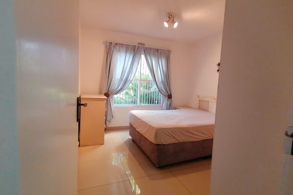 A bedroom featuring tiled flooring, a window with security bars, and a ceiling-mounted light fixture.