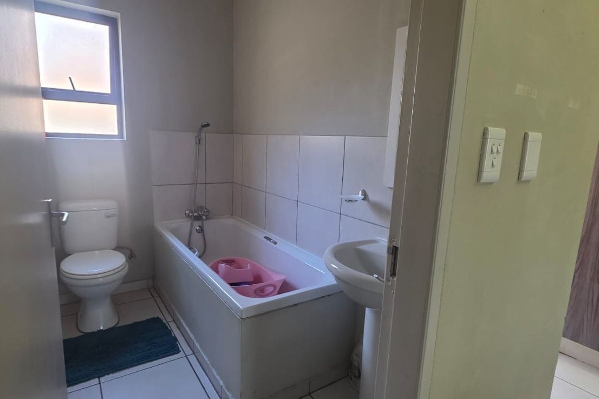 A functional bathroom featuring a standard bathtub with shower mixer, pedestal basin, and toilet, finished with neutral wall tiles.