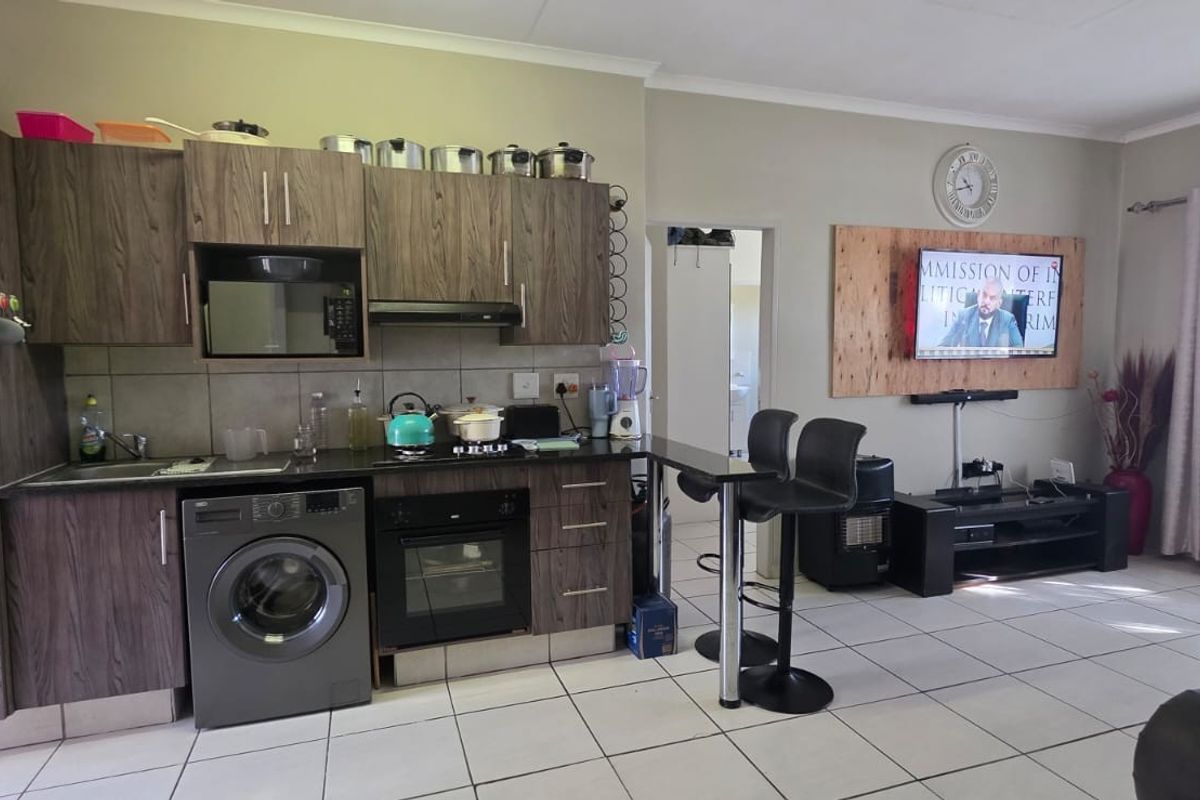 Open-plan living area featuring a compact kitchen with wood-look cabinetry, built-in oven, hob, and extractor fan, seamlessly flowing into the lounge space.