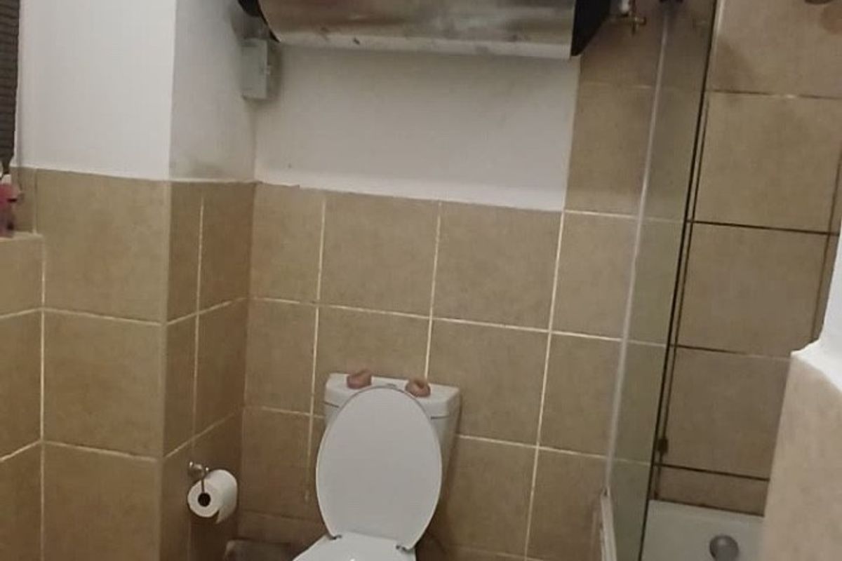 A functional bathroom featuring a toilet, bathtub with glass screen, and exposed water heater tank with visible copper piping.