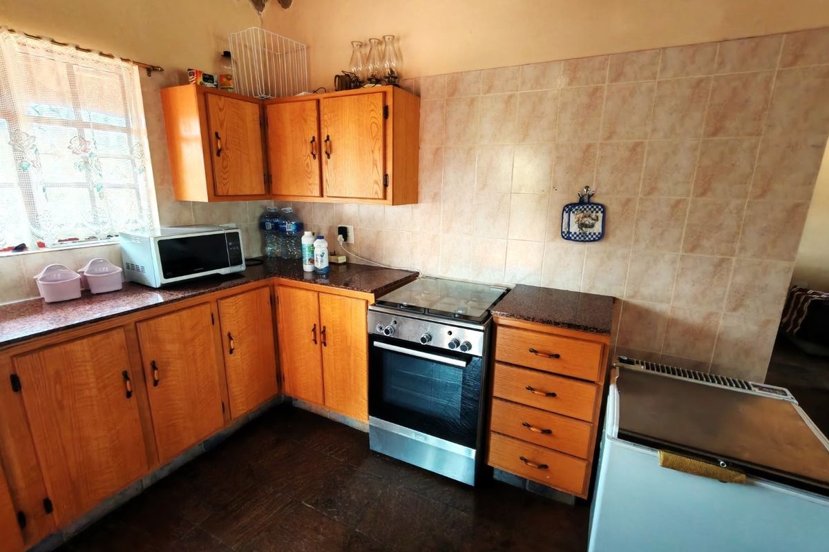 A functional kitchen featuring wooden cabinetry, granite-look countertops, a built-in oven with hob, and tiled wall finishes.