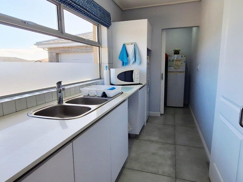 A functional scullery area featuring a double stainless steel sink, white cabinetry, and tiled flooring, providing additional prep and wash-up space.