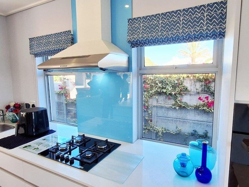 Modern kitchen featuring a gas hob, stainless steel extractor fan, built-in oven, and a sleek glass splashback with ample counter space.