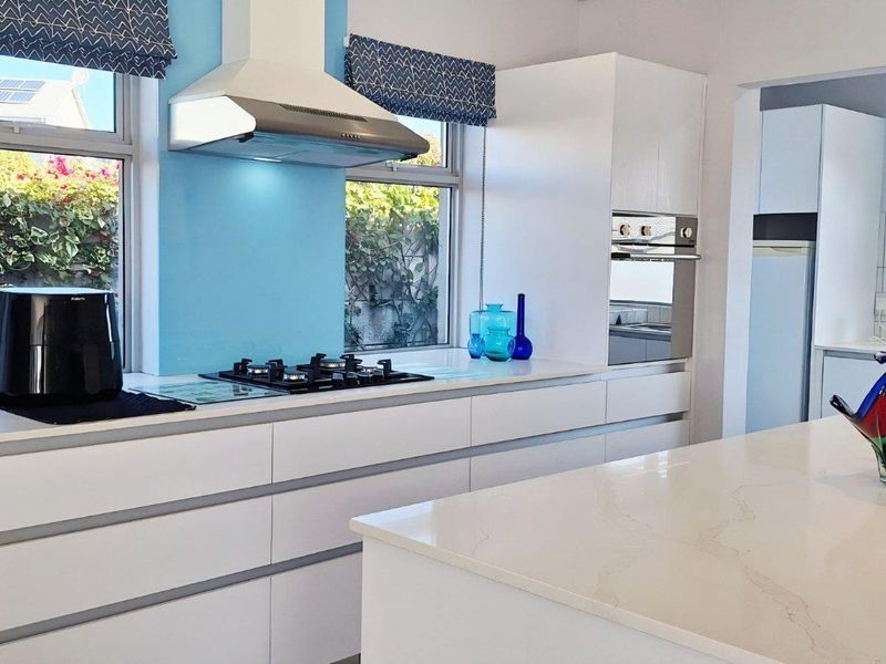 Modern kitchen featuring white cabinetry, stone countertops, a central island, built-in oven, gas hob, and stainless steel extractor fan.