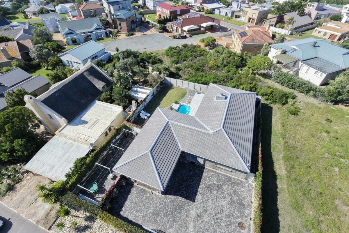 Aerial view of a residential property featuring a tiled roof, paved driveway, private swimming pool, and landscaped garden area within a suburban neighborhood.