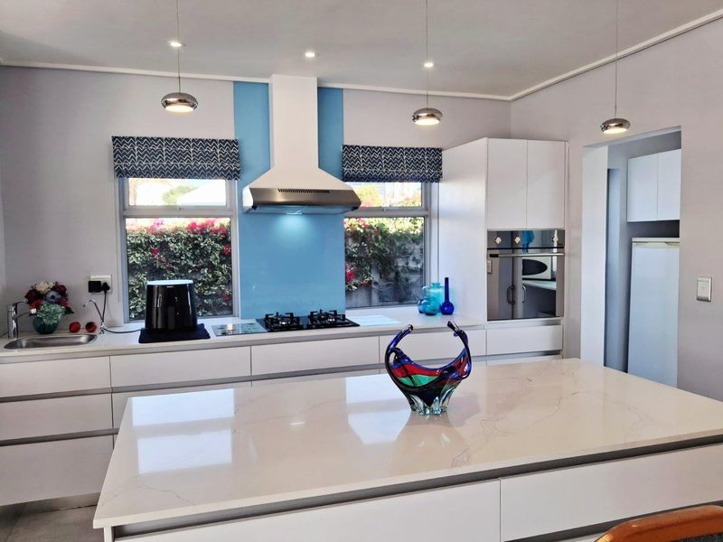 Modern kitchen featuring a central island with stone countertop, built-in oven, gas hob, extractor fan, and sleek cabinetry with a blue glass splashback.