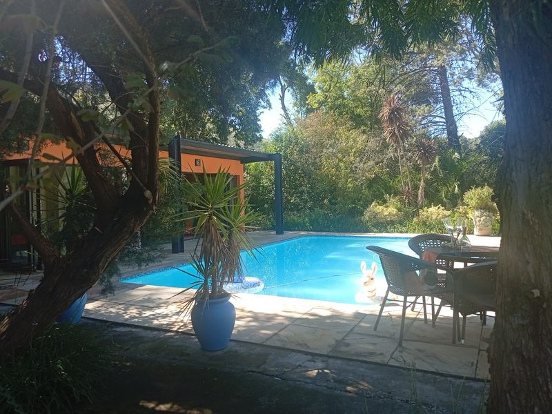 A private outdoor pool area featuring a paved deck, covered patio space, and established garden surroundings, ideal for relaxation and outdoor entertaining.