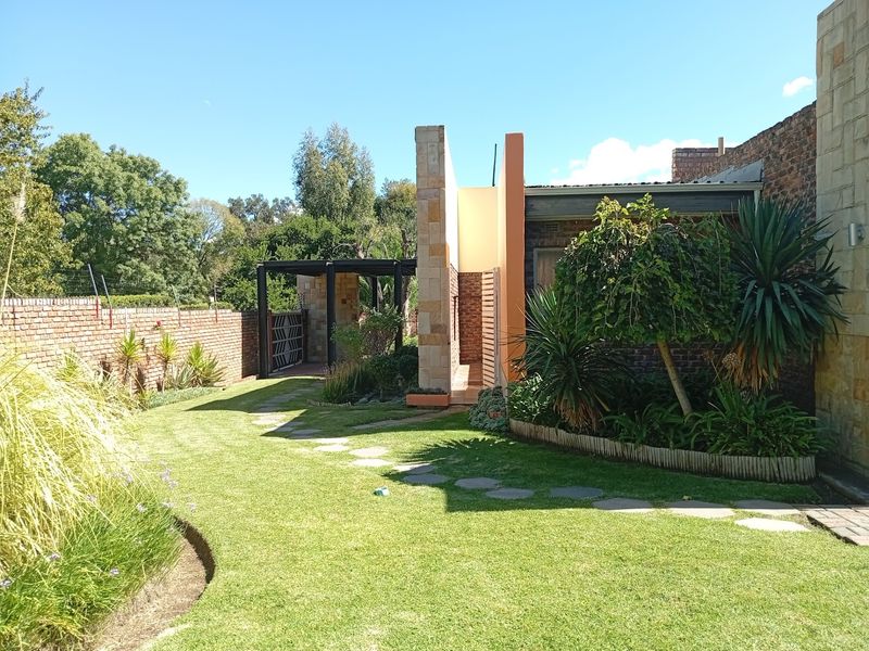 A well-maintained rear garden featuring a manicured lawn, stone pathway, brick boundary wall, and modern architectural facade elements.