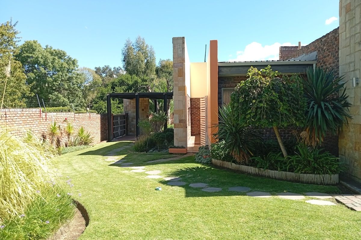A well-maintained rear garden featuring a manicured lawn, stone pathway, brick boundary wall, and modern architectural facade elements.