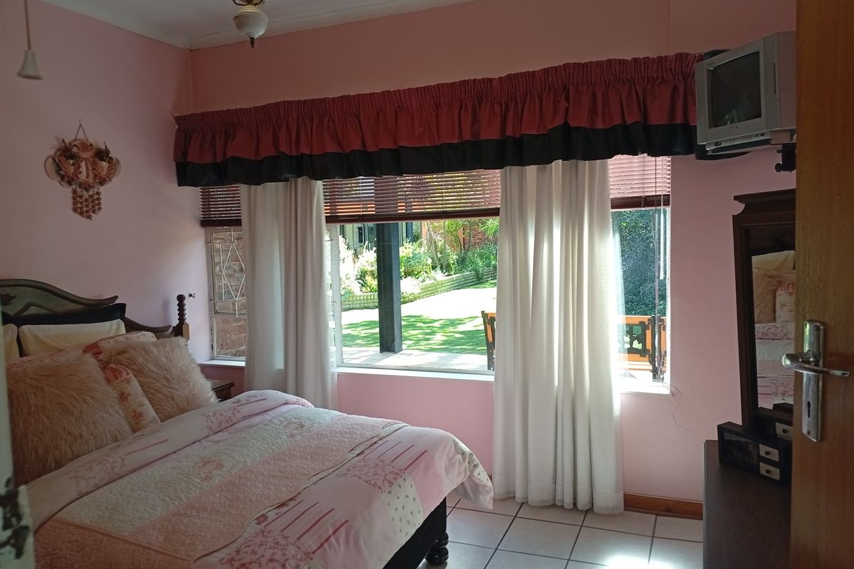 A bedroom featuring tiled flooring and a large window overlooking the garden, providing natural light and outdoor views.
