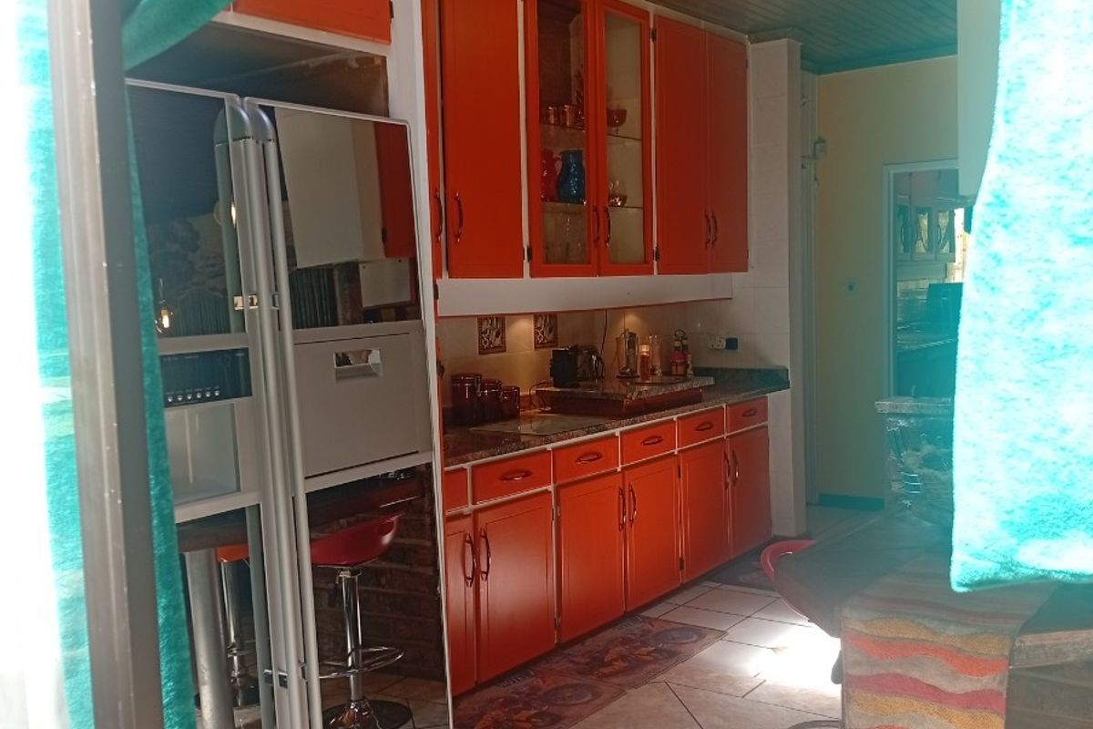 A kitchen featuring vibrant orange cabinetry, tiled flooring, and a timber-paneled ceiling, viewed from an adjacent space.