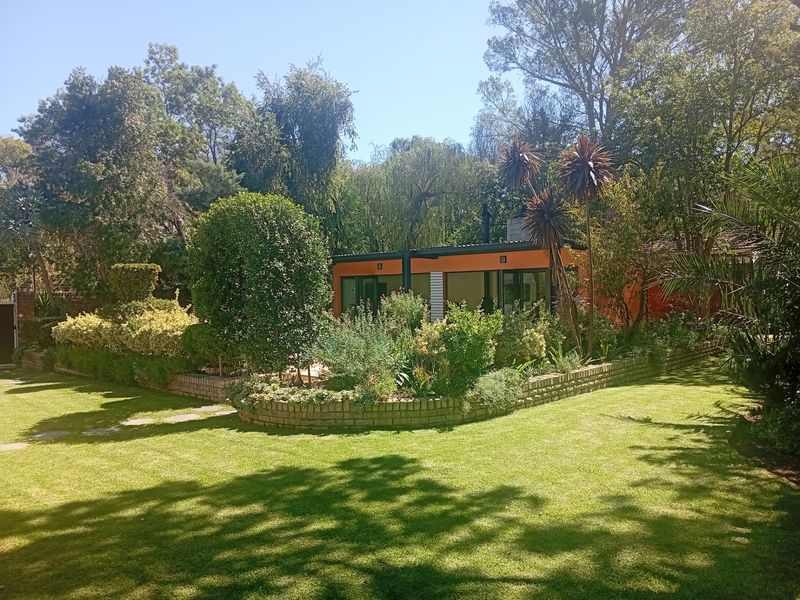 A well-maintained rear garden featuring a lush green lawn, established landscaping, and a modern structure with large glass sliding doors.