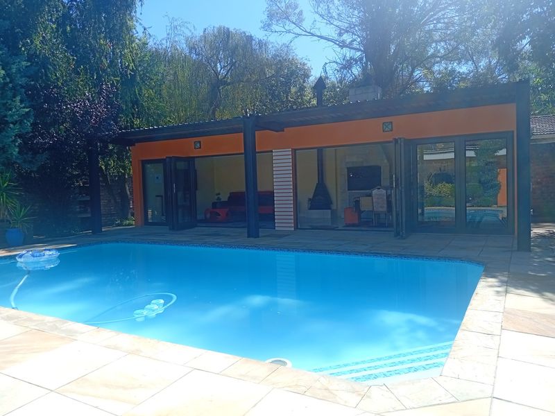 A well-maintained swimming pool area featuring a covered patio with a built-in fireplace, perfect for outdoor entertaining and relaxation.