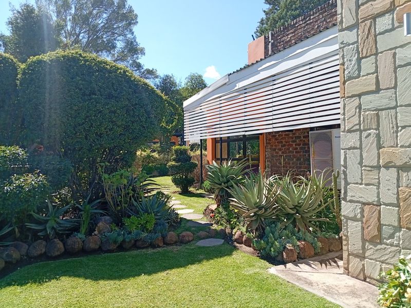 A well-maintained rear garden area featuring stone cladding, a paved pathway, and a covered patio structure with white louvred screening.