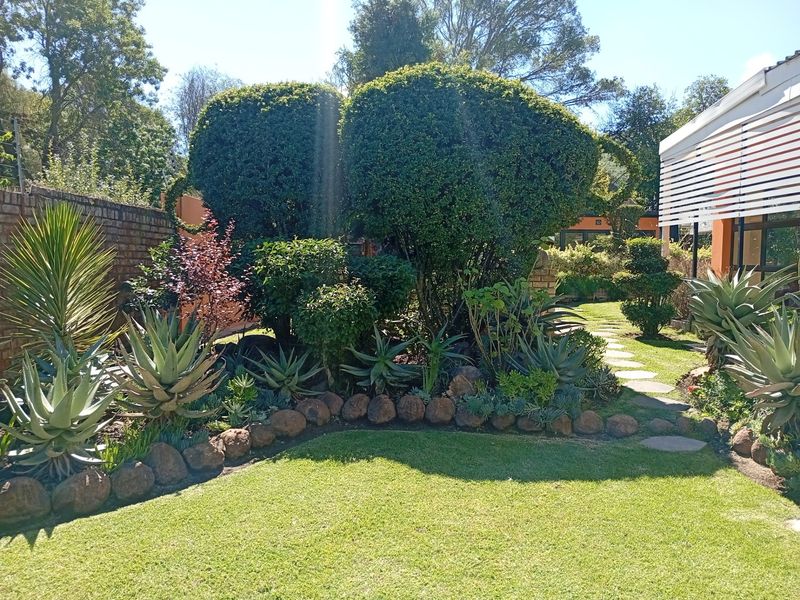 A well-maintained rear garden featuring a manicured lawn, established shrubbery, stone-bordered garden beds, and a paved pathway leading through the outdoor space.
