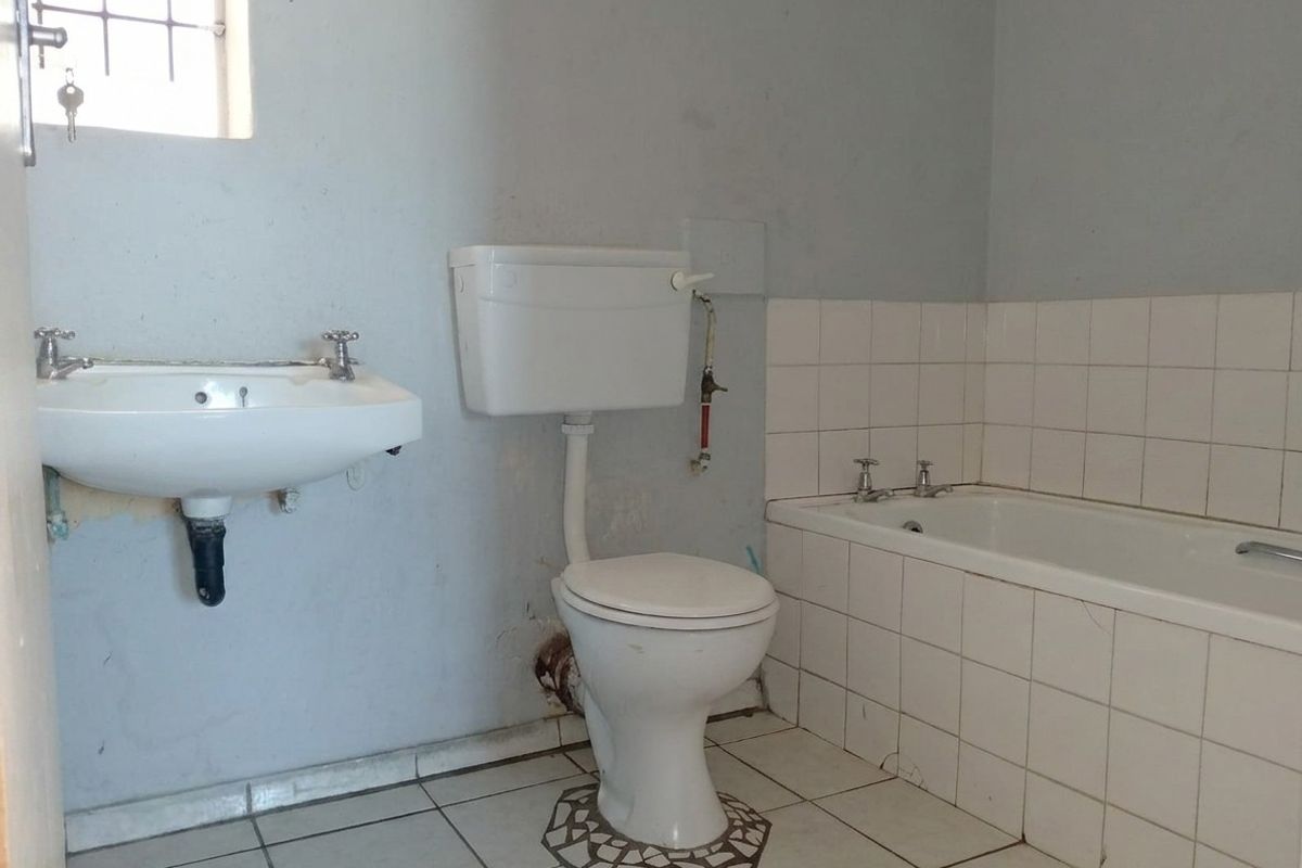 A dated bathroom featuring a standard bathtub, wall-mounted basin, and toilet, requiring cosmetic updates and maintenance to improve its overall condition.