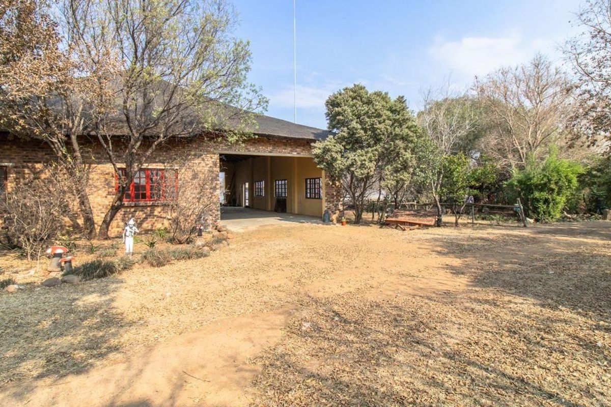 Rear view of a rustic brick building with a thatched roof, featuring a large open-sided covered patio area and surrounding natural garden space.