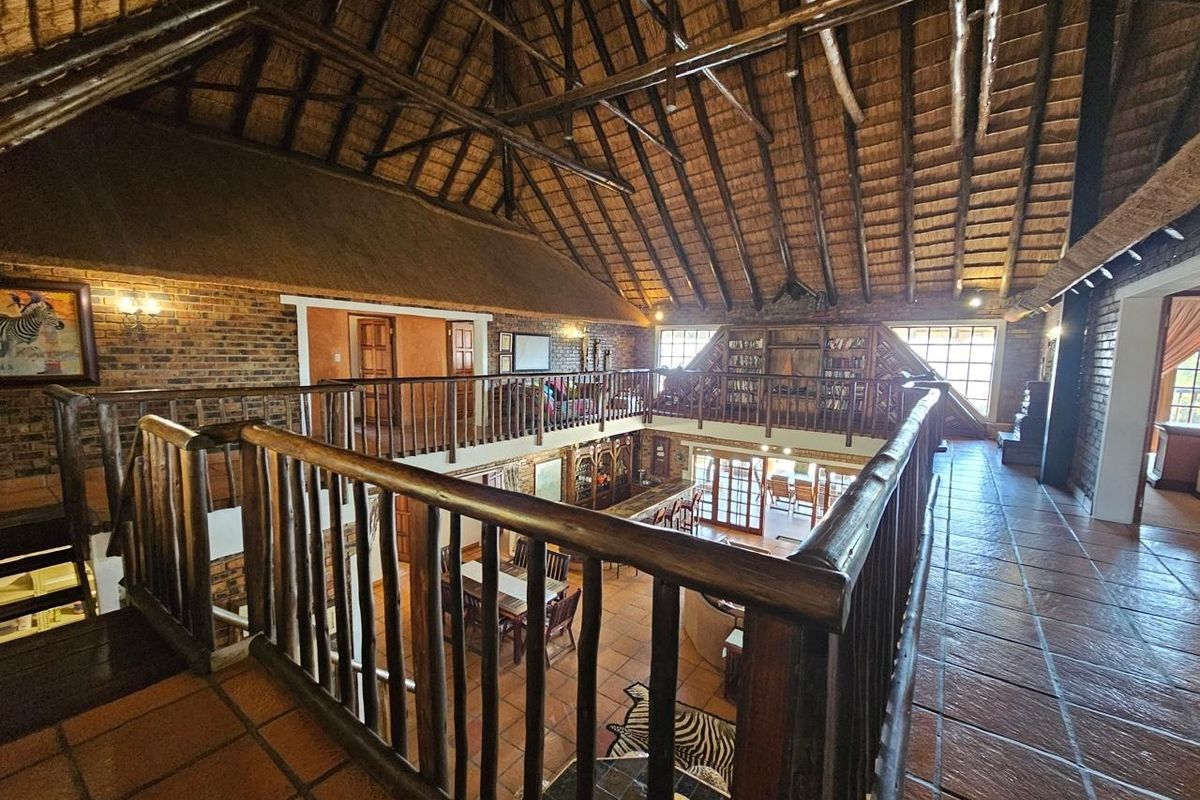 Spacious mezzanine living area featuring high exposed thatch ceilings, timber trusses, and rustic brickwork overlooking the main floor living space.