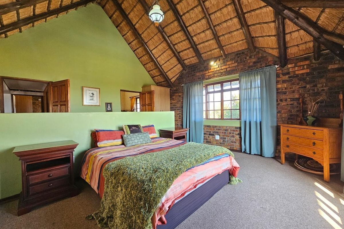 Spacious bedroom featuring a high vaulted thatched ceiling with exposed timber rafters, exposed brickwork, and a partition wall creating a semi-private layout.