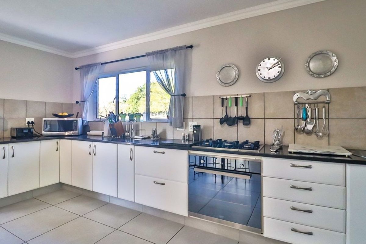 A functional kitchen featuring white cabinetry, dark countertops, a built-in oven, gas hob, and tiled splashbacks with a window overlooking the exterior.