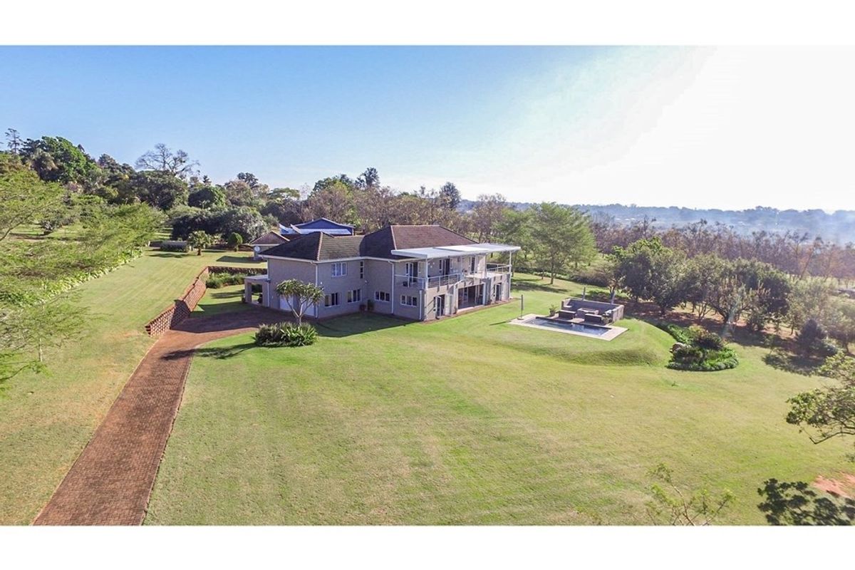 Aerial view of a large residential property featuring a spacious lawn, swimming pool, and a multi-level house with a balcony.