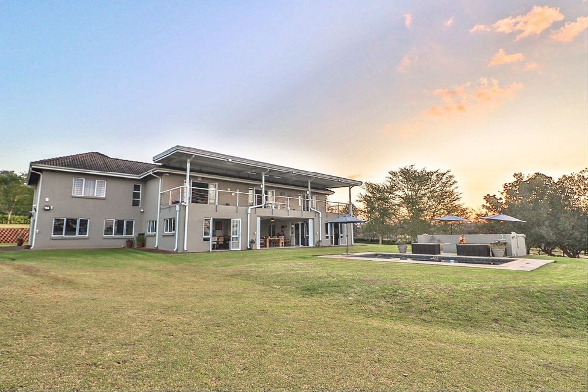 Spacious rear exterior view featuring a large lawn, swimming pool, covered patio, and balcony, showcasing the property's expansive outdoor living and entertainment space.
