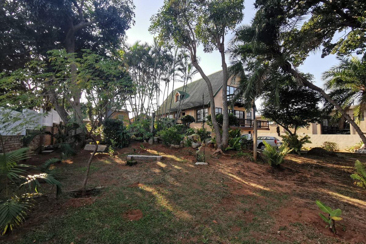 A view of the rear garden and property exterior, featuring mature trees, landscaped greenery, and a multi-level house structure.