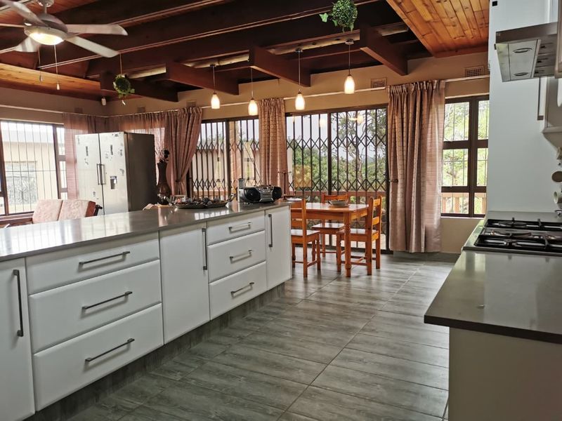 Spacious open-plan kitchen and dining area featuring a large central island, modern cabinetry, tiled flooring, and exposed timber beam ceilings.