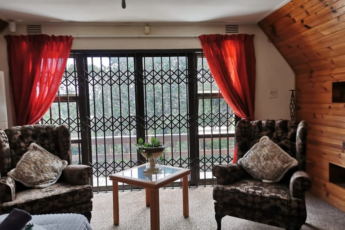 A living area featuring a large sliding door with security gate, wood-paneled wall, and carpeted flooring.