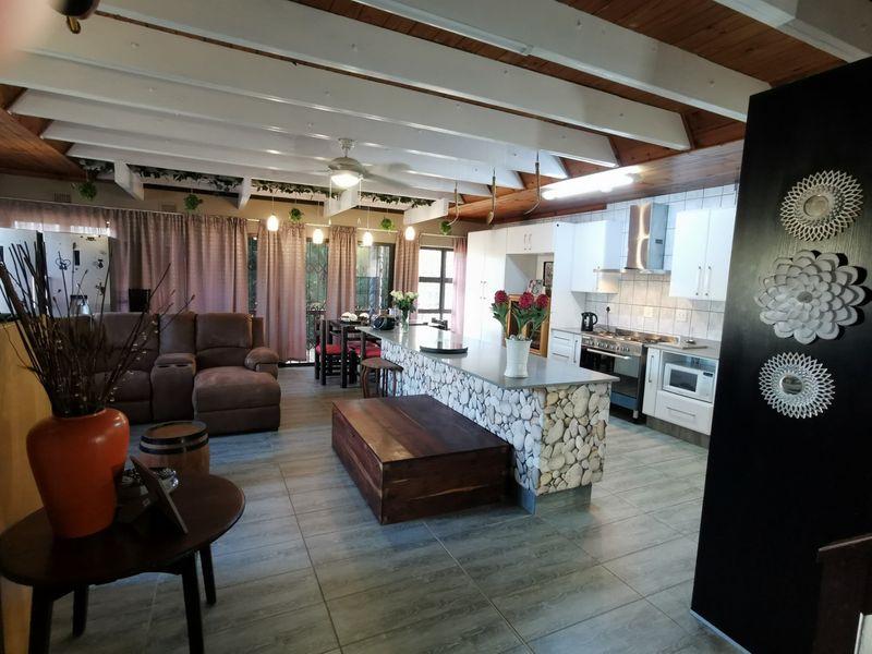 Open-plan living and kitchen area featuring a stone-clad breakfast island, exposed timber ceiling beams, and tiled flooring throughout.