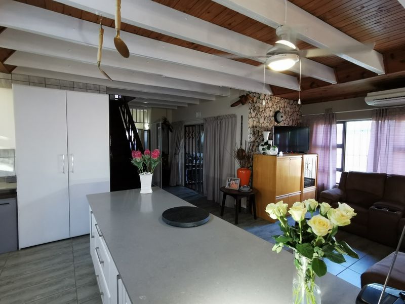 Open plan living area featuring a kitchen island with stone countertop, exposed timber beam ceiling, and stone feature wall.