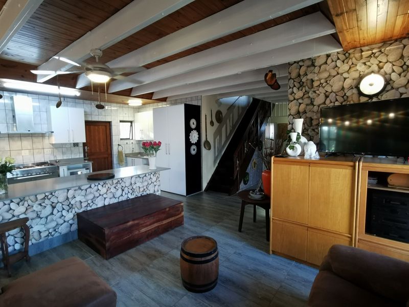 Open plan living area featuring a kitchen with stone-clad breakfast bar, exposed timber beam ceiling, and a feature stone wall with staircase.