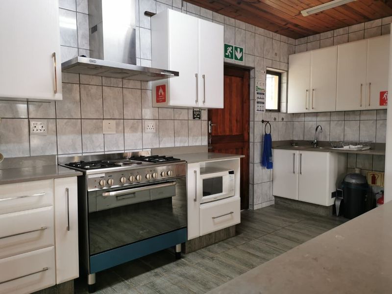 A functional kitchen featuring white cabinetry, a stainless steel gas stove with extractor fan, tiled splashbacks, and a timber-paneled ceiling.