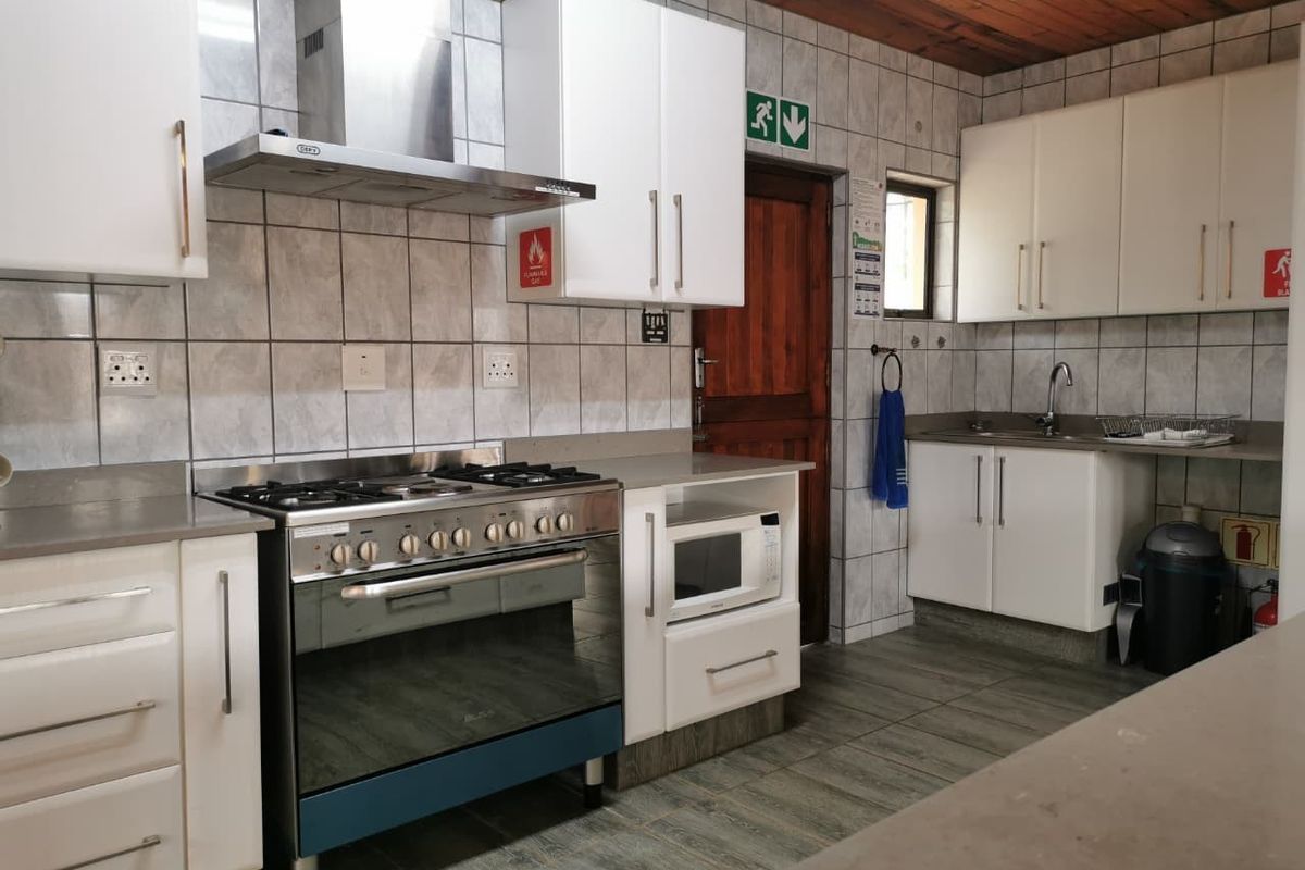 A functional kitchen featuring white cabinetry, a stainless steel gas stove with extractor fan, tiled splashbacks, and a timber-paneled ceiling.