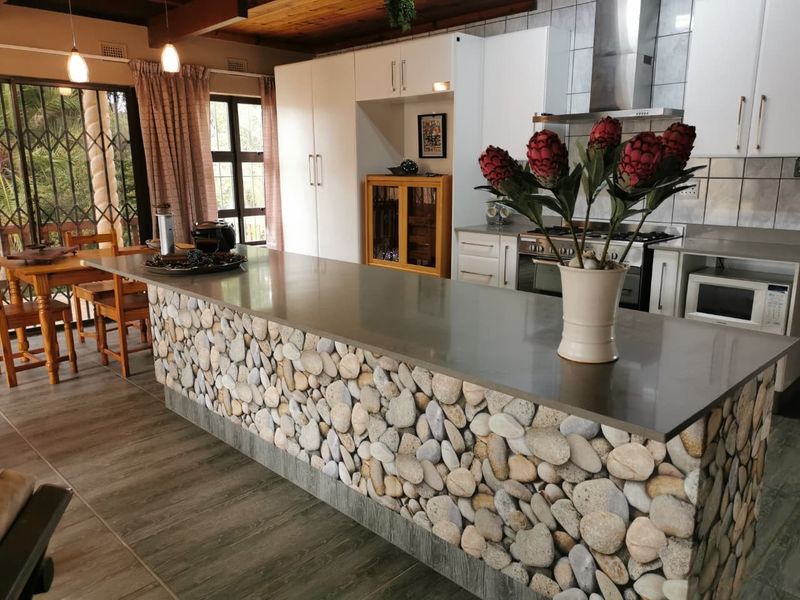 Open plan kitchen featuring a large stone-clad island, white cabinetry, stainless steel extractor fan, and integrated oven, flowing into the dining area.