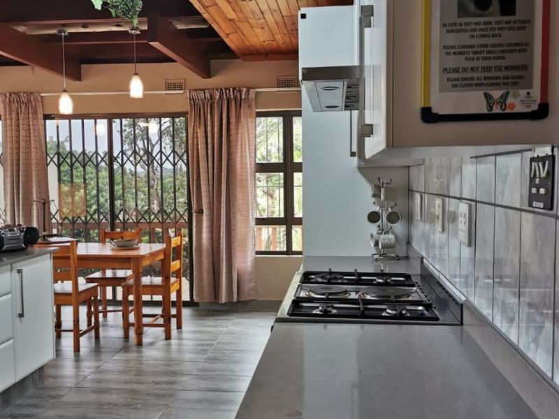Open plan kitchen and dining area featuring a gas hob, extractor fan, tiled flooring, and exposed timber beam ceiling with sliding door access.