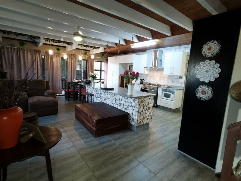 Open plan living and kitchen area featuring a stone-clad breakfast island, white cabinetry, stainless steel extractor fan, and exposed timber beam ceiling.