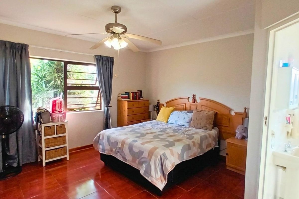 A bedroom featuring tiled flooring, a ceiling fan, and an adjoining en-suite bathroom area.